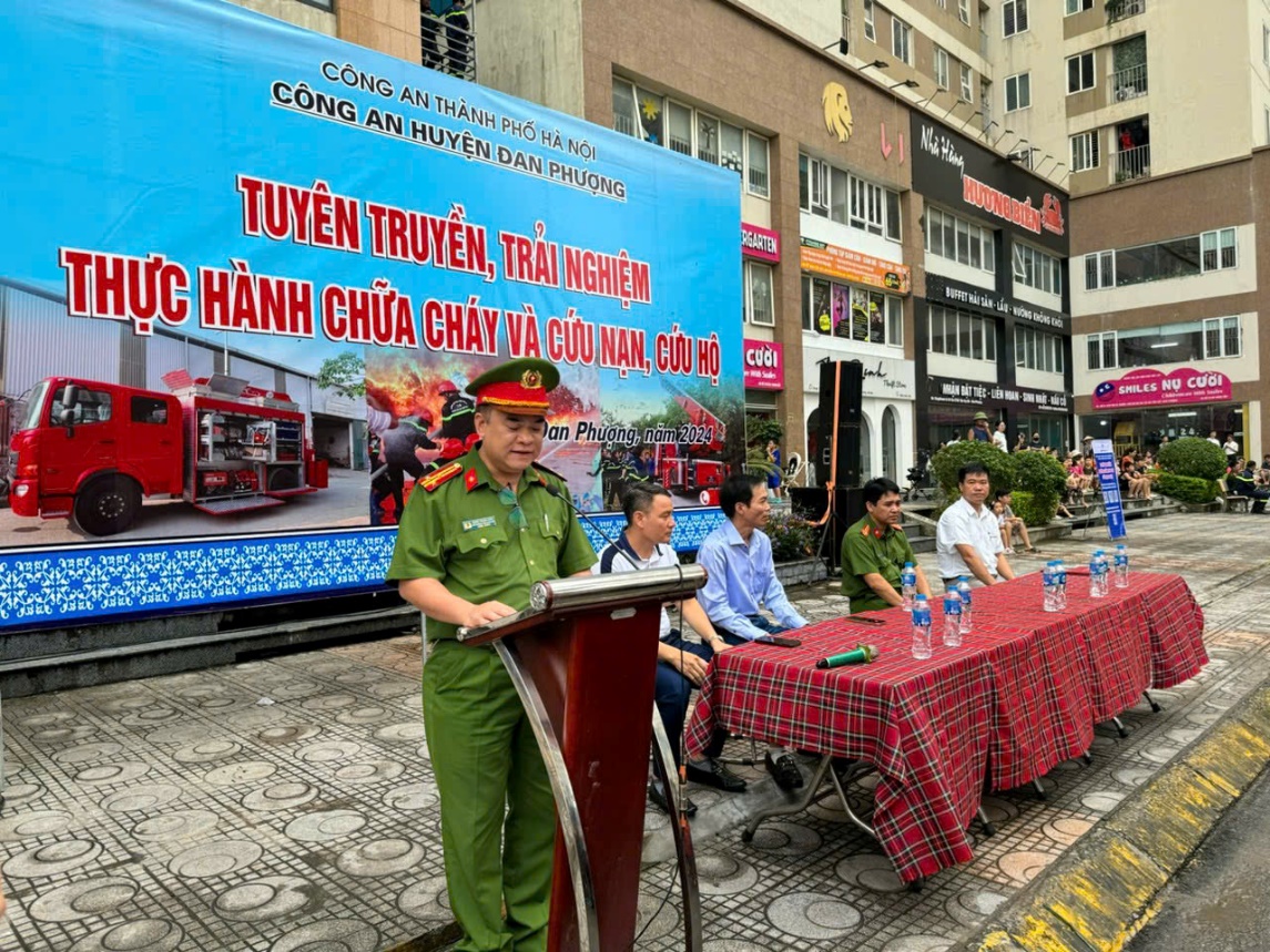 A person in uniform standing at a podium with a table with drinks and a sign  Description automatically generated