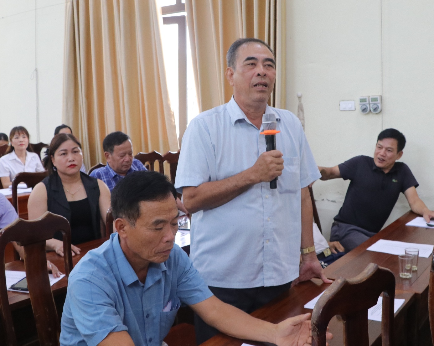 A person holding a microphone in front of a group of people  AI-generated content may be incorrect.