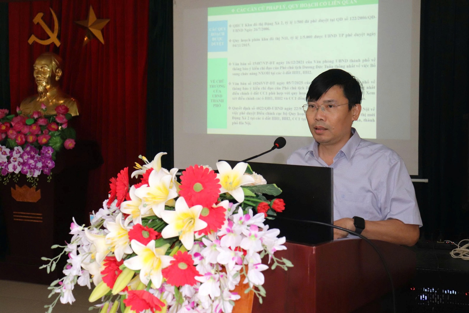 A person sitting at a podium with a microphone and flowers  AI-generated content may be incorrect.