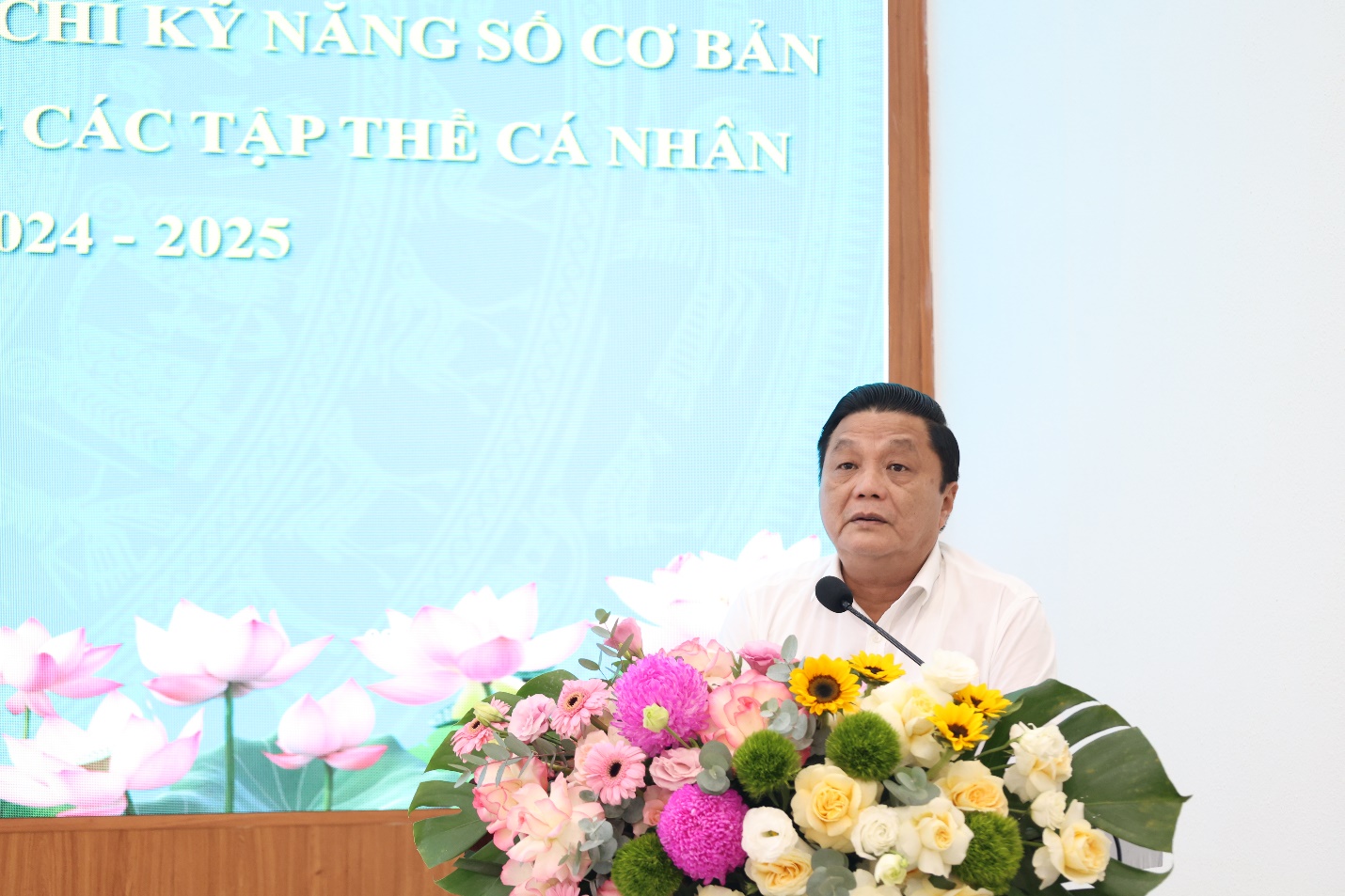 A person standing at a podium with a microphone and flowers  AI-generated content may be incorrect.