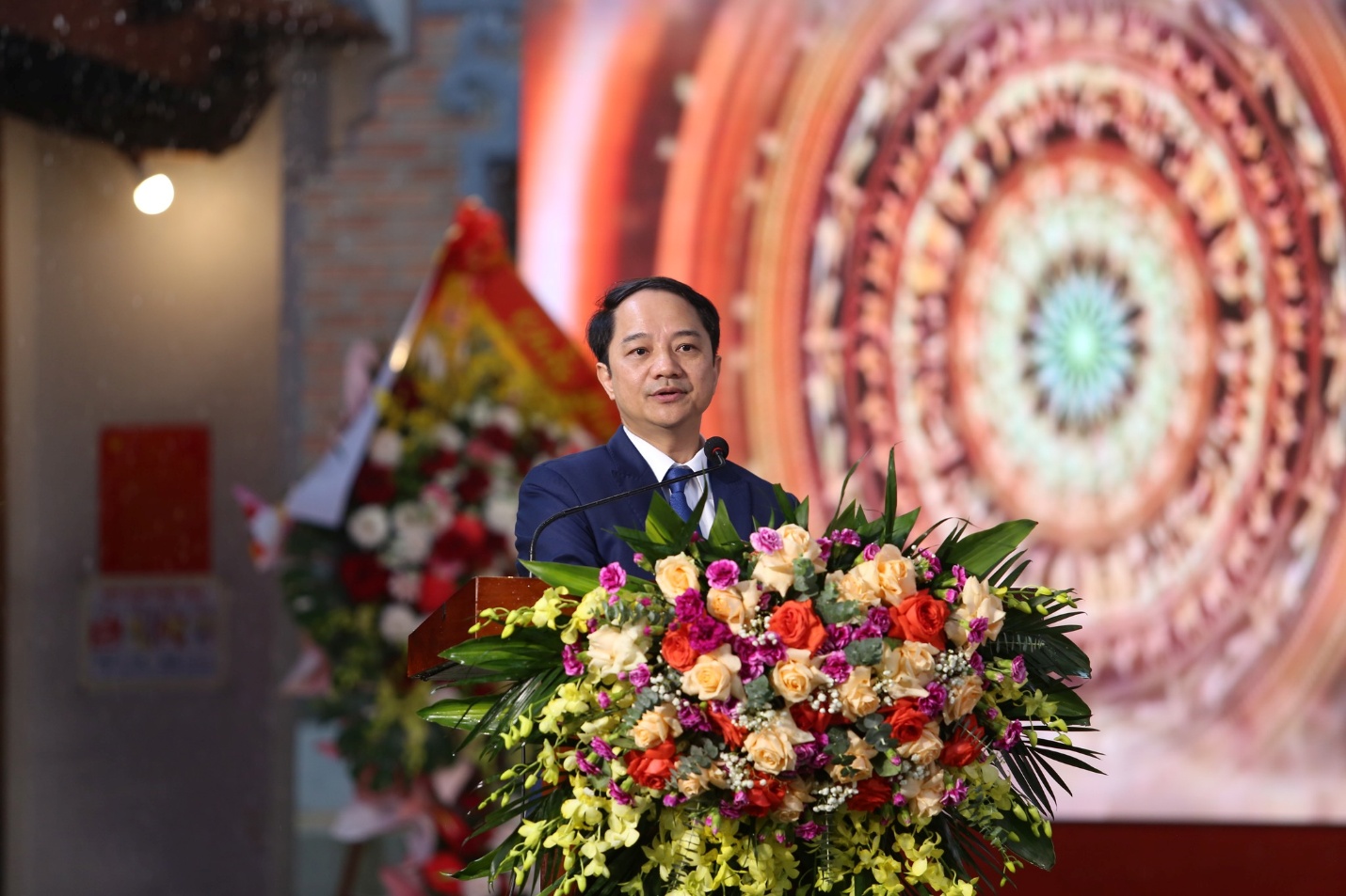 A person standing behind a podium with a bouquet of flowers  Description automatically generated