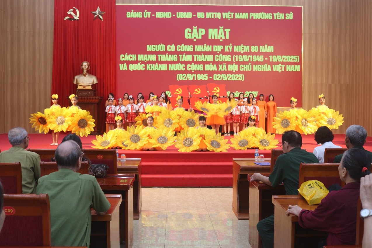 A group of people sitting in chairs in front of a stage with a stage with yellow flowers  AI-generated content may be incorrect.