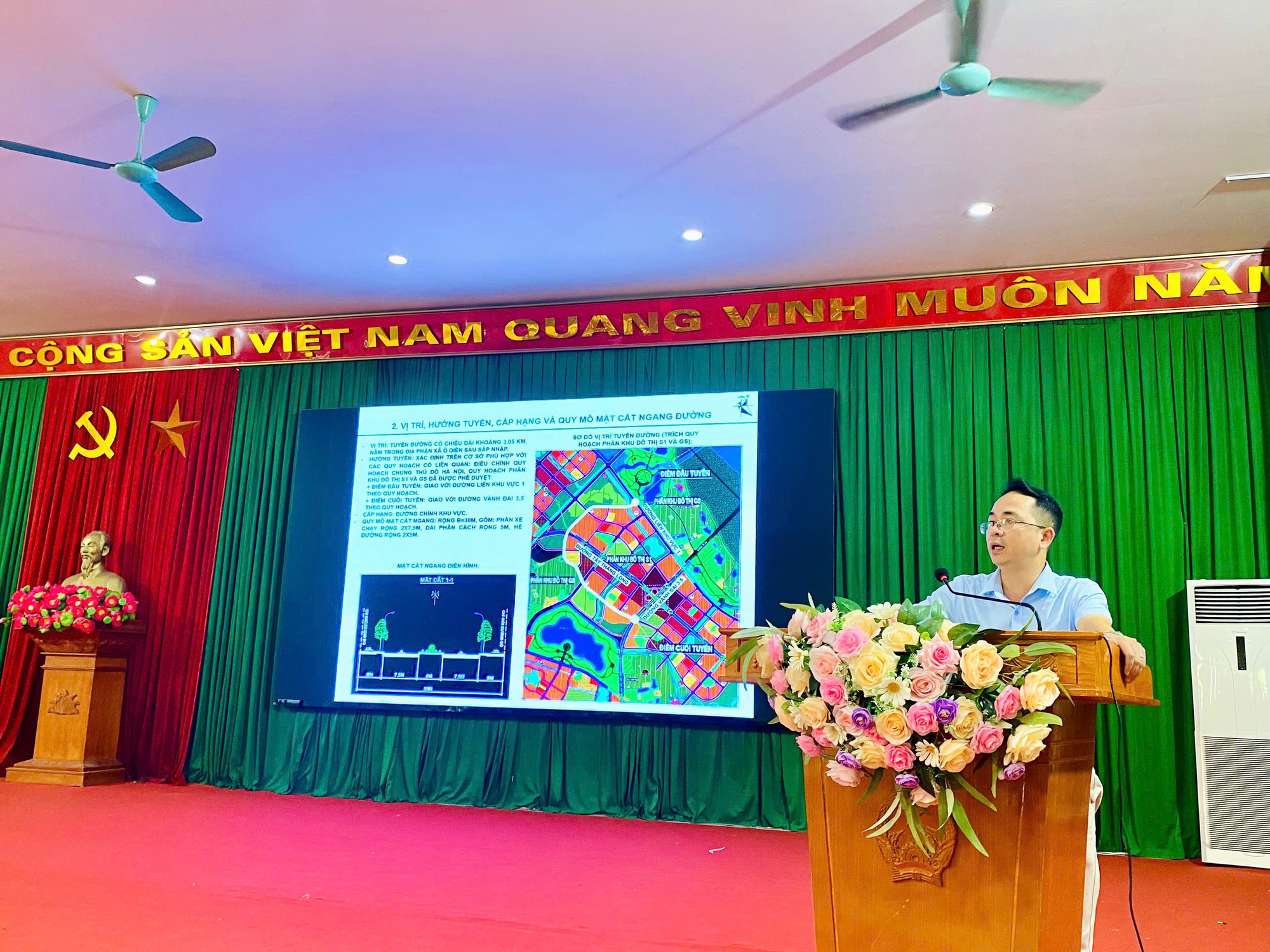 A person standing at a podium with a large screen  Description automatically generated