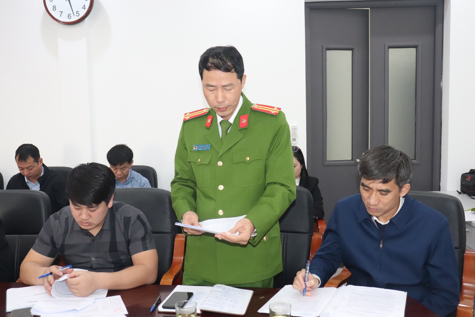 A person in a green uniform standing in front of a group of people  AI-generated content may be incorrect.