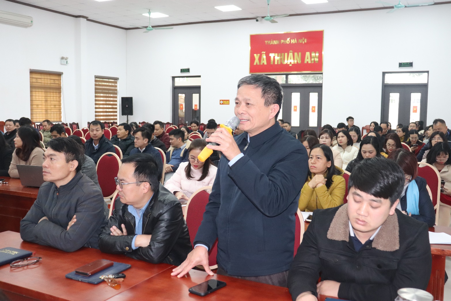 A person speaking into a microphone in a room with people seated  AI-generated content may be incorrect.