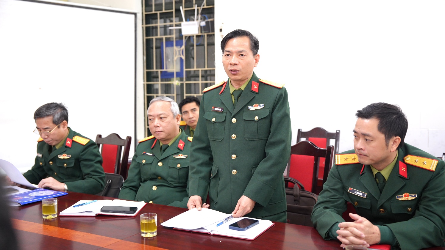 A person in military uniform standing in front of several men sitting at a table  AI-generated content may be incorrect.