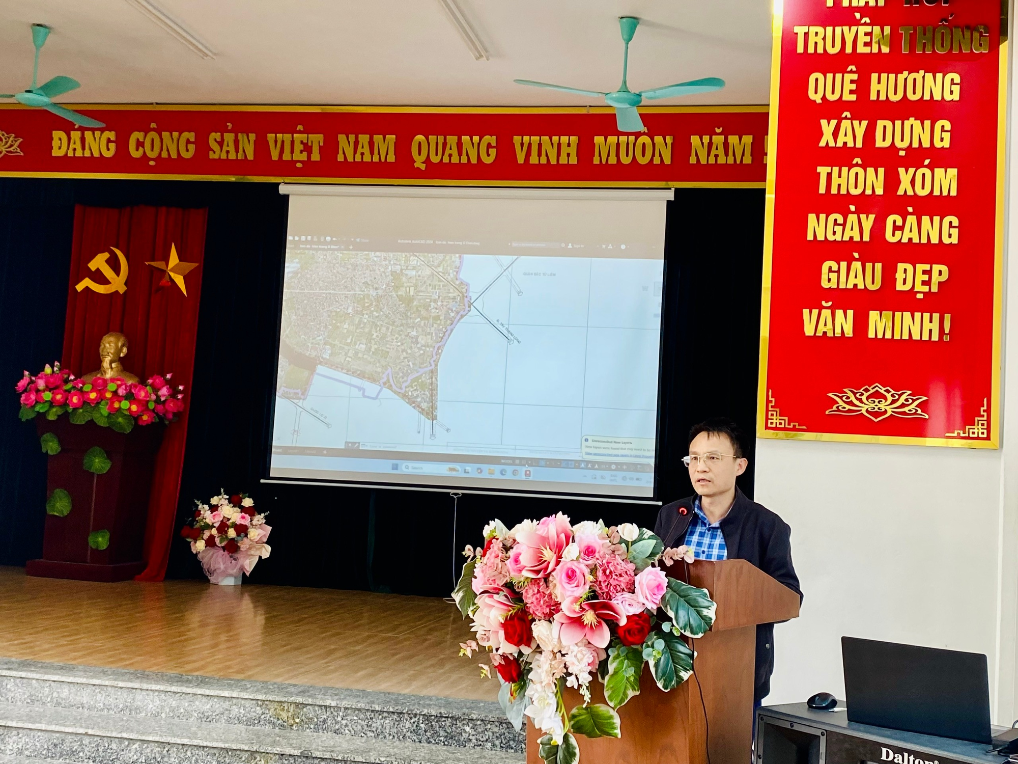 A person standing at a podium with flowers on the stage  Description automatically generated