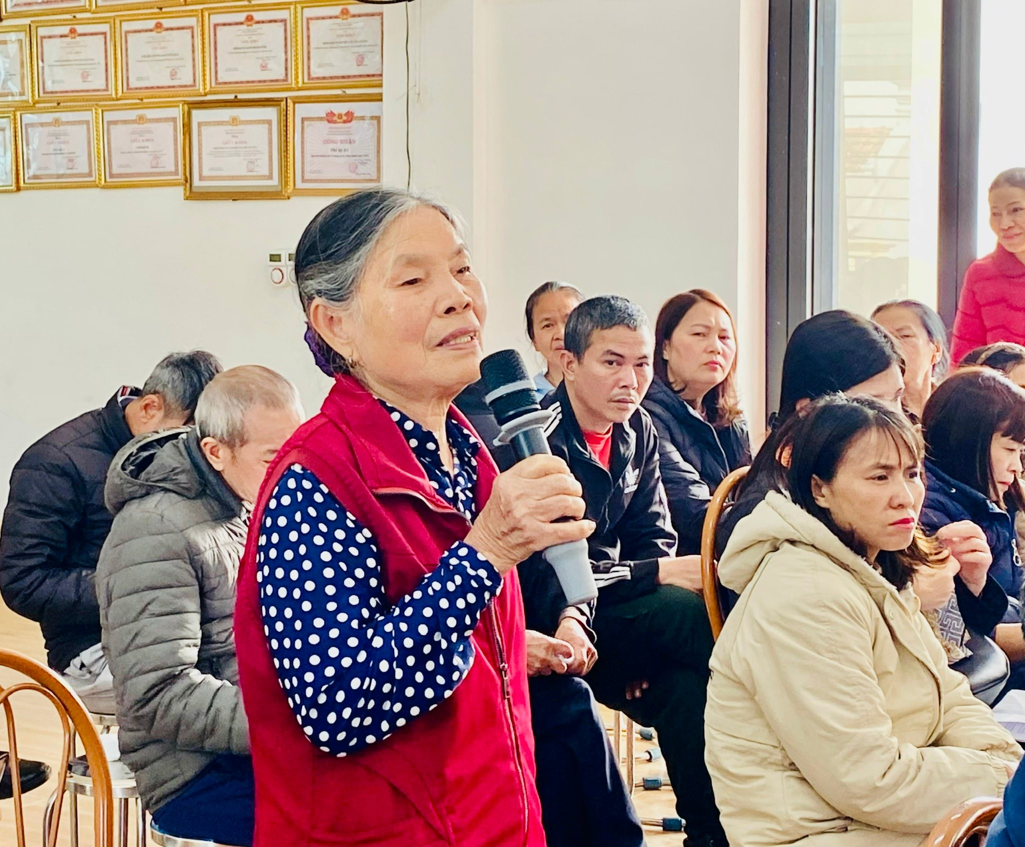 A person holding a microphone in front of a group of people  Description automatically generated