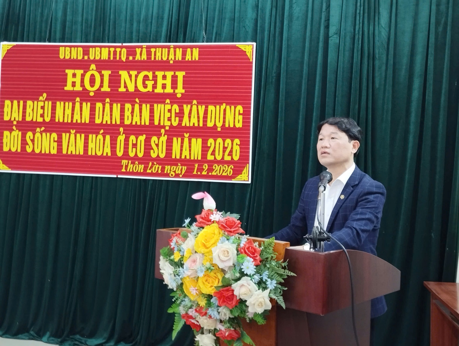 A person standing at a podium with a microphone and flowers  AI-generated content may be incorrect.