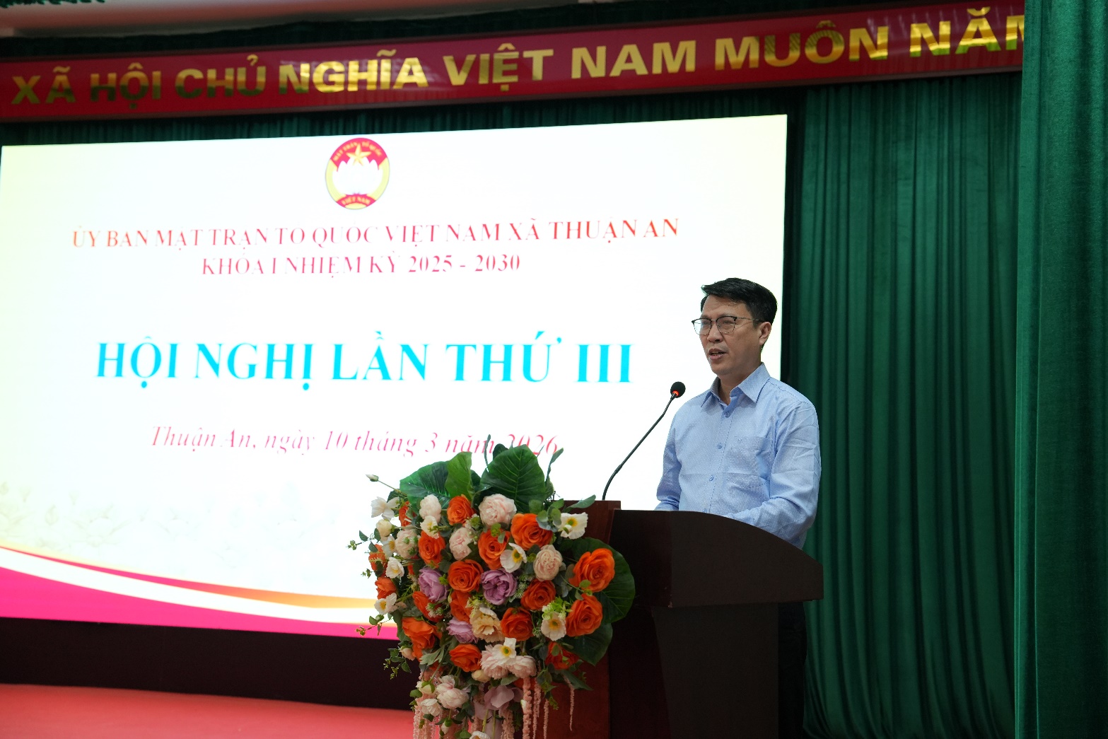 A person standing at a podium with a microphone and flowers  AI-generated content may be incorrect.