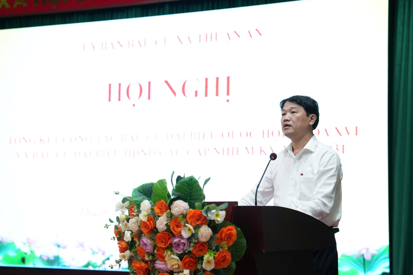 A person standing at a podium with a microphone and flowers  AI-generated content may be incorrect.