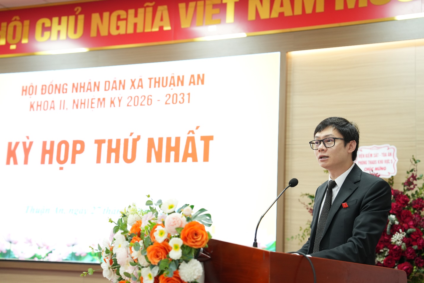 A person standing at a podium with a microphone and flowers  AI-generated content may be incorrect.