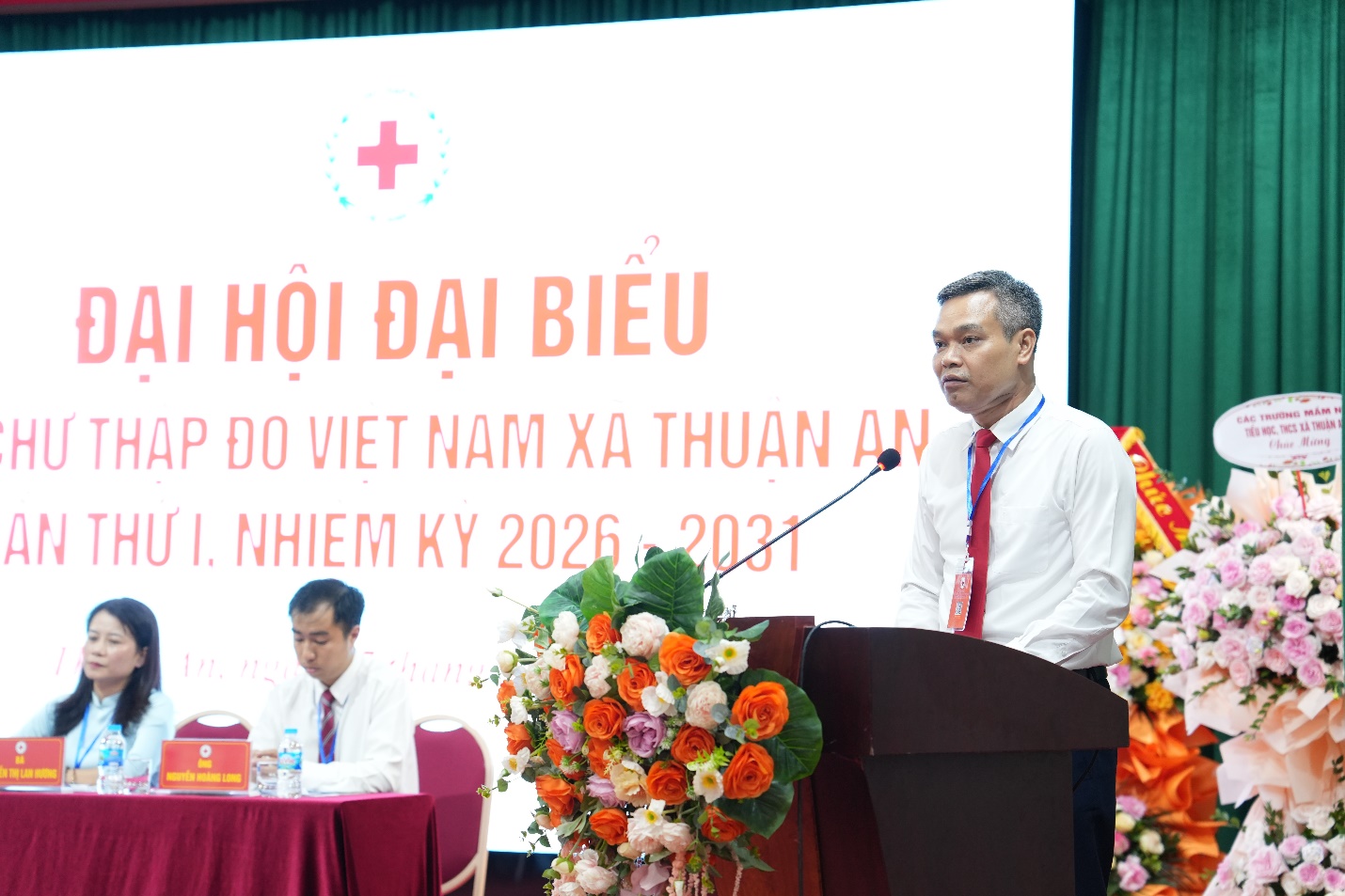 A person standing at a podium with a microphone and flowers  AI-generated content may be incorrect.