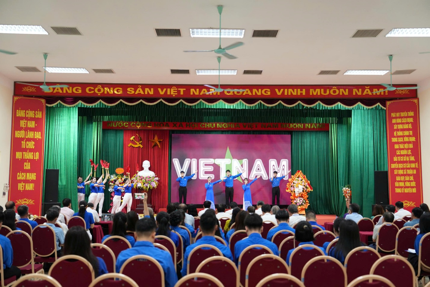 A group of people in a room with a stage and a stage with a fan  AI-generated content may be incorrect.