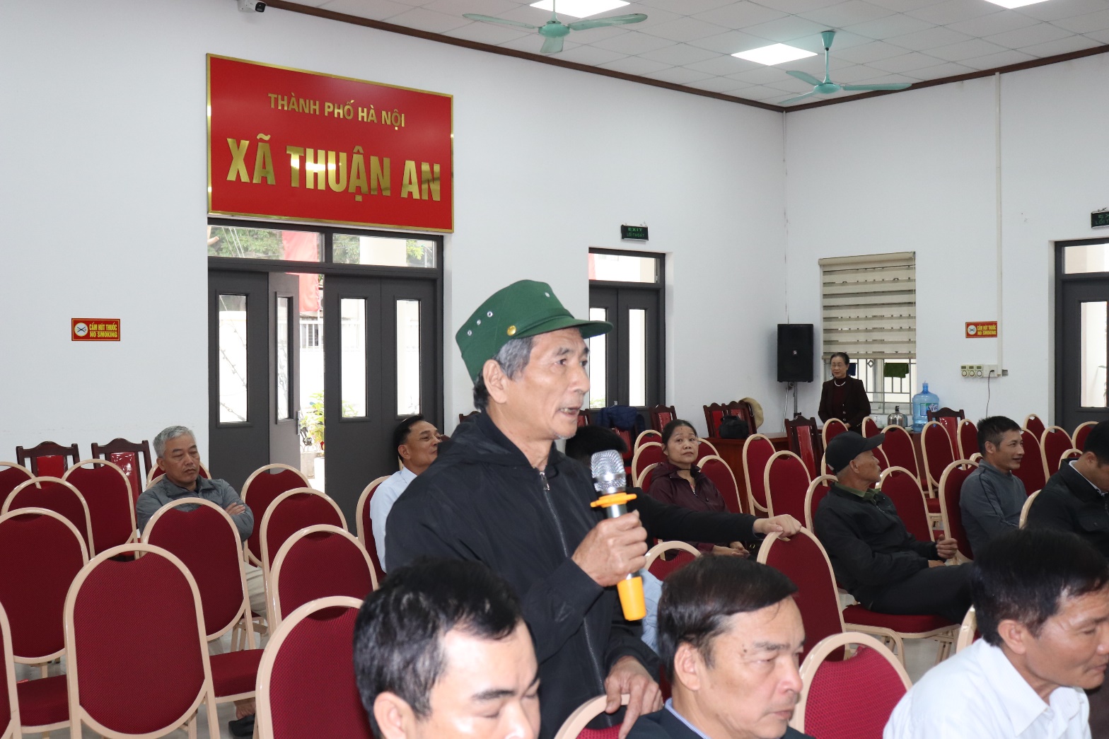 A person holding a microphone in a room with people sitting in chairs  AI-generated content may be incorrect.