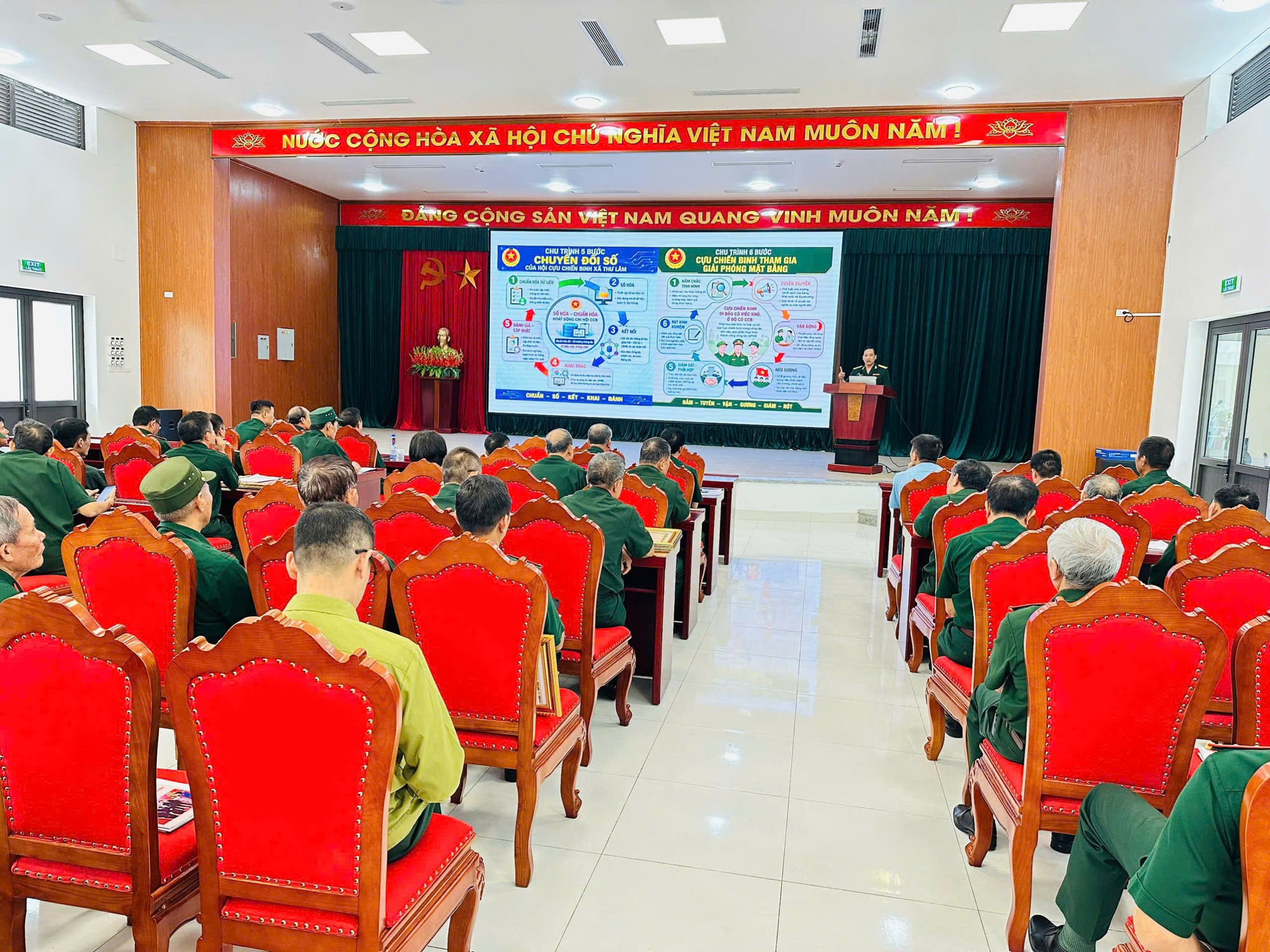 The image shows a classroom setting with a large, decorated room, a podium, and a group of people, likely students, seated in rows. There is a presentation being given, with a slide showing information about Vietnamese cuisine and cultural events.  AI-generated content may be incorrect.