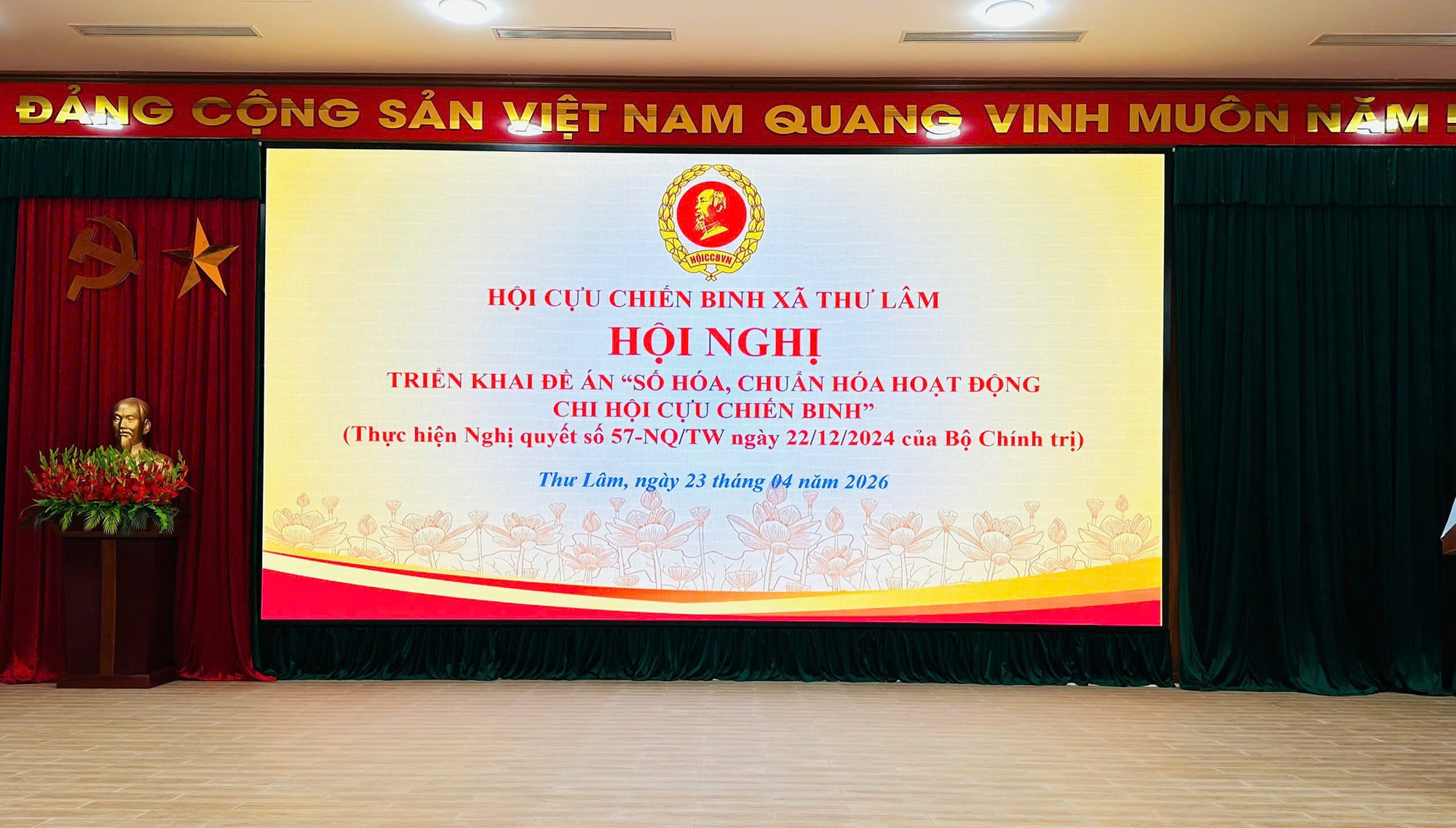 The image depicts a presentation in a large hall with a red banner featuring the Vietnamese flag, a speaker, and a Vietnamese text about an award ceremony.  AI-generated content may be incorrect.