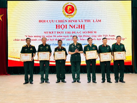 The image depicts a group of Vietnamese military personnel, dressed in uniform, standing in a ceremonial setting with decorations and flags, including a red flag and a yellow flag, symbolizing a significant historical or commemorative event.  AI-generated content may be incorrect.