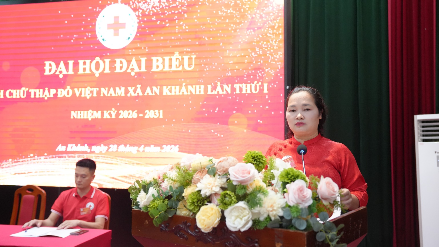 A person standing at a podium with a microphone and flowers  AI-generated content may be incorrect.