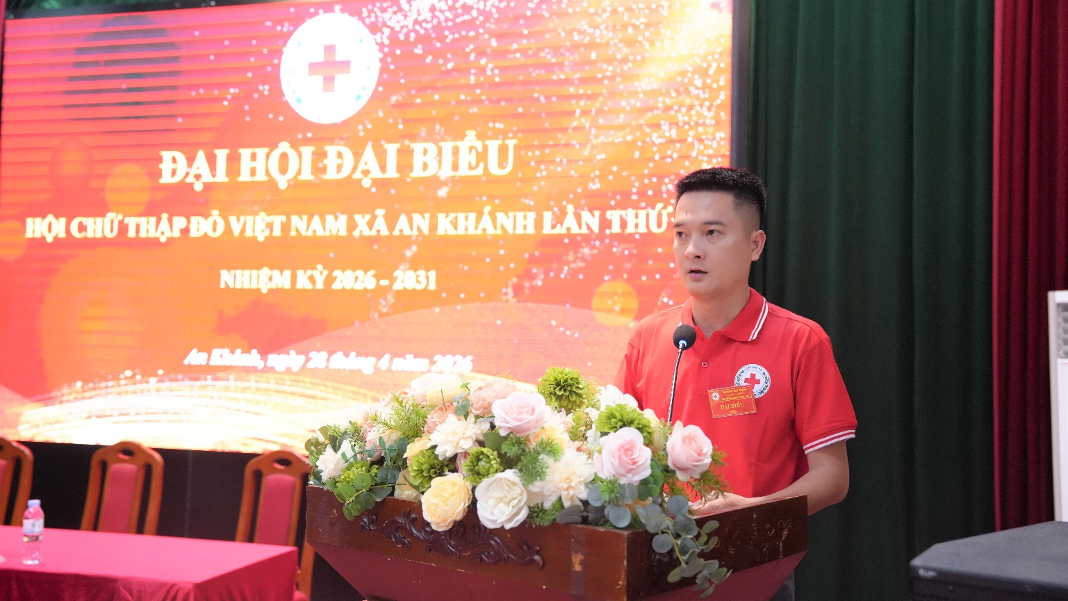 A person standing at a podium with a microphone and flowers  AI-generated content may be incorrect.