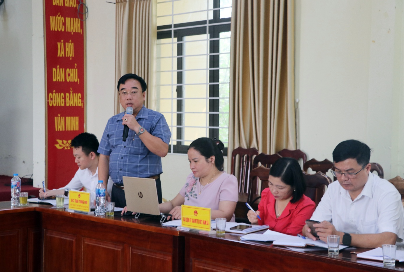 A person speaking into a microphone while a group of people sit at a table  AI-generated content may be incorrect.