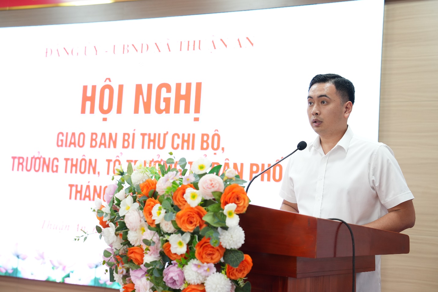 A person standing at a podium with a microphone and flowers  AI-generated content may be incorrect.