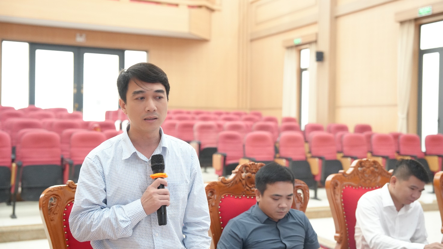 A person holding a microphone in front of another person sitting in chairs  AI-generated content may be incorrect.