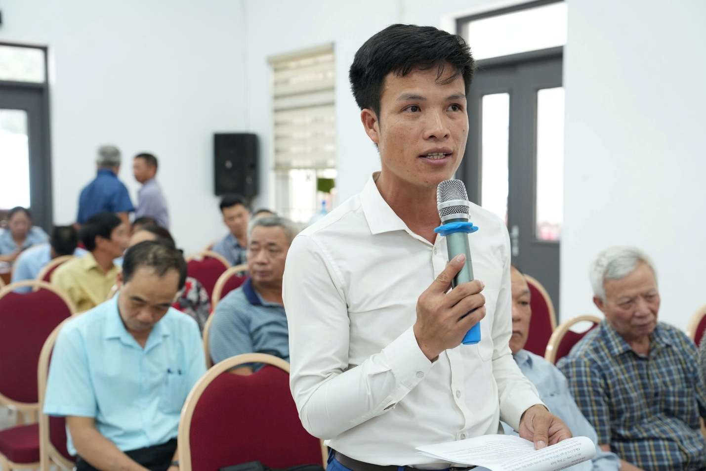 A person holding a microphone in front of a group of people  AI-generated content may be incorrect.